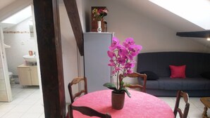 A dining area with a round table covered in a pink tablecloth, surrounded by wooden chairs, and a potted orchid plant in the center. - 4-person apartment (Docelles)