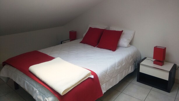 A bedroom with a sloped ceiling, a bed with red and white bedding, two bedside tables with red lamps, and a white throw blanket on the bed. - 4-person apartment (Docelles)