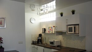 Een compacte keuken met witte kastjes, een magnetron, een broodrooster en een koffiezetapparaat. Op het aanrecht staat een kleine prullenbak en een potplant.