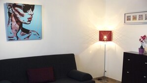 Een woonkamer met een zwarte bank, een witte salontafel, een vloerlamp en een schilderij aan de muur.