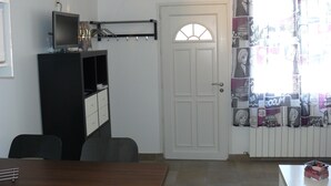 Een kamer met een witte deur, een televisie op een standaard, een klein tafeltje en een raam met gordijnen met een patroon.