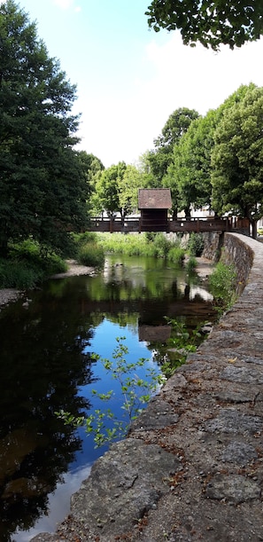 A stone bridge over a calm river, surrounded by lush greenery and a small wooden structure.