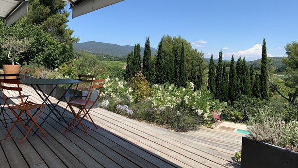 A wooden deck with outdoor furniture, a pool, and a scenic view of trees and hills.