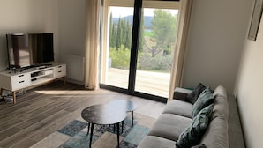 A modern living room with a sofa, a coffee table, a TV, and a sliding glass door leading to an outdoor deck.