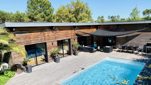 Ein moderner Poolbereich im Freien mit Holzterrasse, integriertem Sitzbereich und überdachter Terrasse.