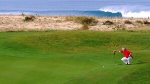 Ein Golfplatz mit Blick auf das Meer, und eine Person im roten Hemd spielt Golf.