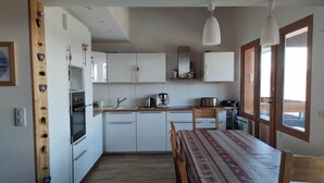 Una cocina moderna con armarios blancos, una mesa de comedor de madera y lámparas colgantes.