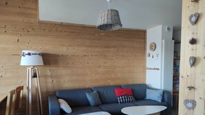 Una sala de estar moderna con pared de madera, un sofá azul, una mesa blanca y una lámpara de pie.