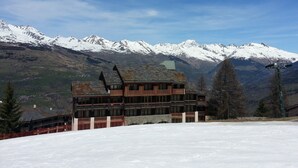 Un edificio de varios pisos con techo inclinado, rodeado de montañas nevadas y un cielo despejado.