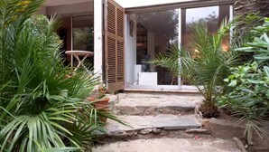 A stone pathway leading to a sliding glass door, surrounded by lush greenery and a small seating area.