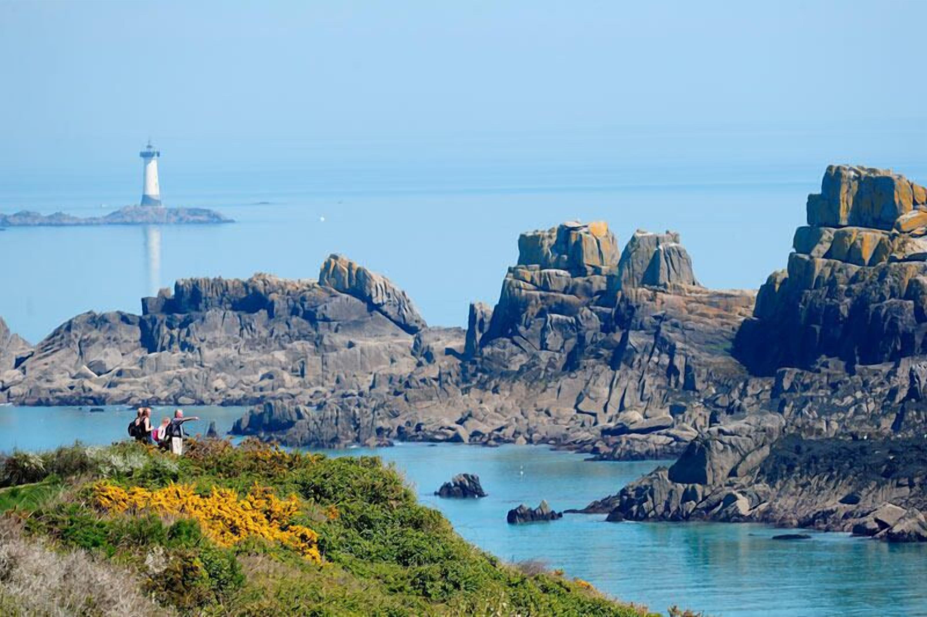 A coastal landscape with rocky formations and a lighthouse in the distance.