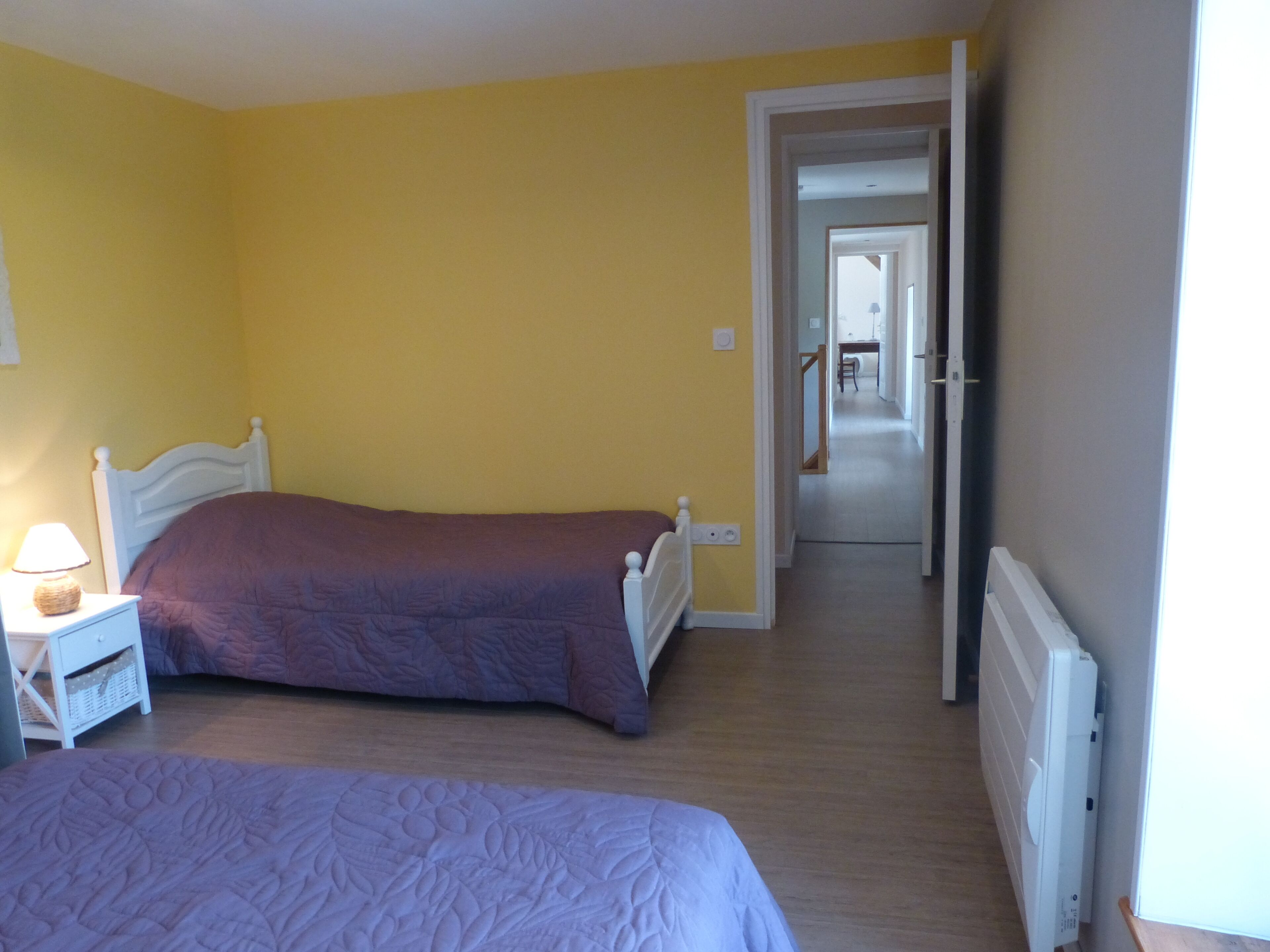 A room with two beds, a nightstand with a lamp, and a radiator.