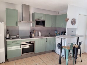 Een kleine keuken met een magnetron, oven en vaatwasser. Er is een spoelbak met een kraan, en een tafeltje met stoelen.