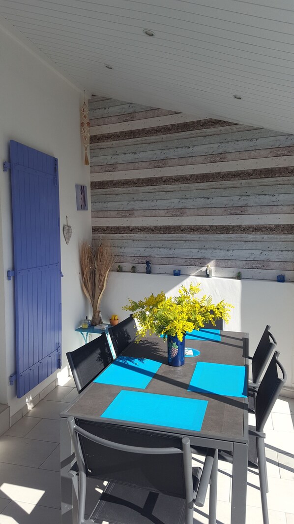 A dining area with a table set for four, blue placemats, and a vase with yellow flowers. - Air-conditioned villa, free WIFI, 500 m from the beach in residence with swimming pool. (Portiragnes)