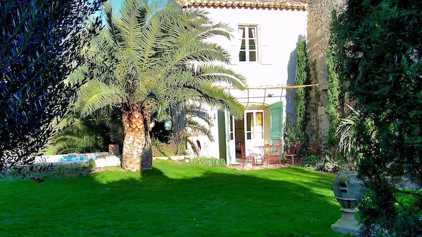 A white building with a tiled roof, a small pool, and a well-maintained lawn.