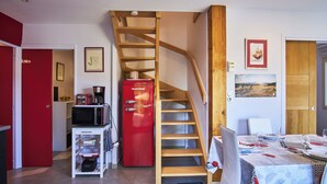 Un espacio habitable compacto con una escalera de madera, un refrigerador rojo, un comedor y una pequeña cocina con microondas.