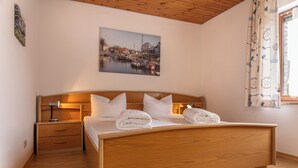 A neatly made bed with pillows and folded towels, a bedside lamp, a wooden nightstand, and a painting of a harbor scene on the wall. - Spacious and bright: the first floor apartment with its spacious bathroom is equipped with a (Carolinensiel)