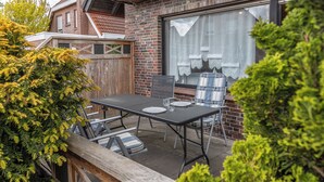 A patio with a table and chairs, a wooden fence, and a brick building with a window. - Spacious and bright: the first floor apartment with its spacious bathroom is equipped with a (Carolinensiel)