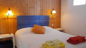 Ett hotellrum med en väggpanel av trä, en säng med ett blått sänggavel, två väggmonterade lampor och ett fönster som släpper in naturligt ljus.