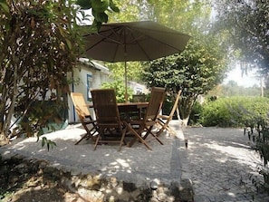 Une terrasse extérieure avec une table et des chaises, entourée de verdure et avec un bâtiment en arrière-plan.