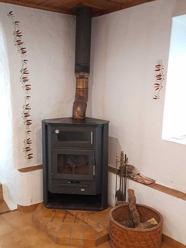 A wood-burning stove in a corner of a room with white walls and a window.