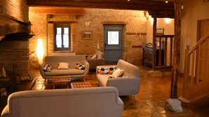 A cozy living room with a fireplace, stone walls, and wooden beams. There are two sofas and a coffee table.