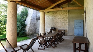 An outdoor covered patio with a long wooden table and chairs, stone pillars, and a blue door.