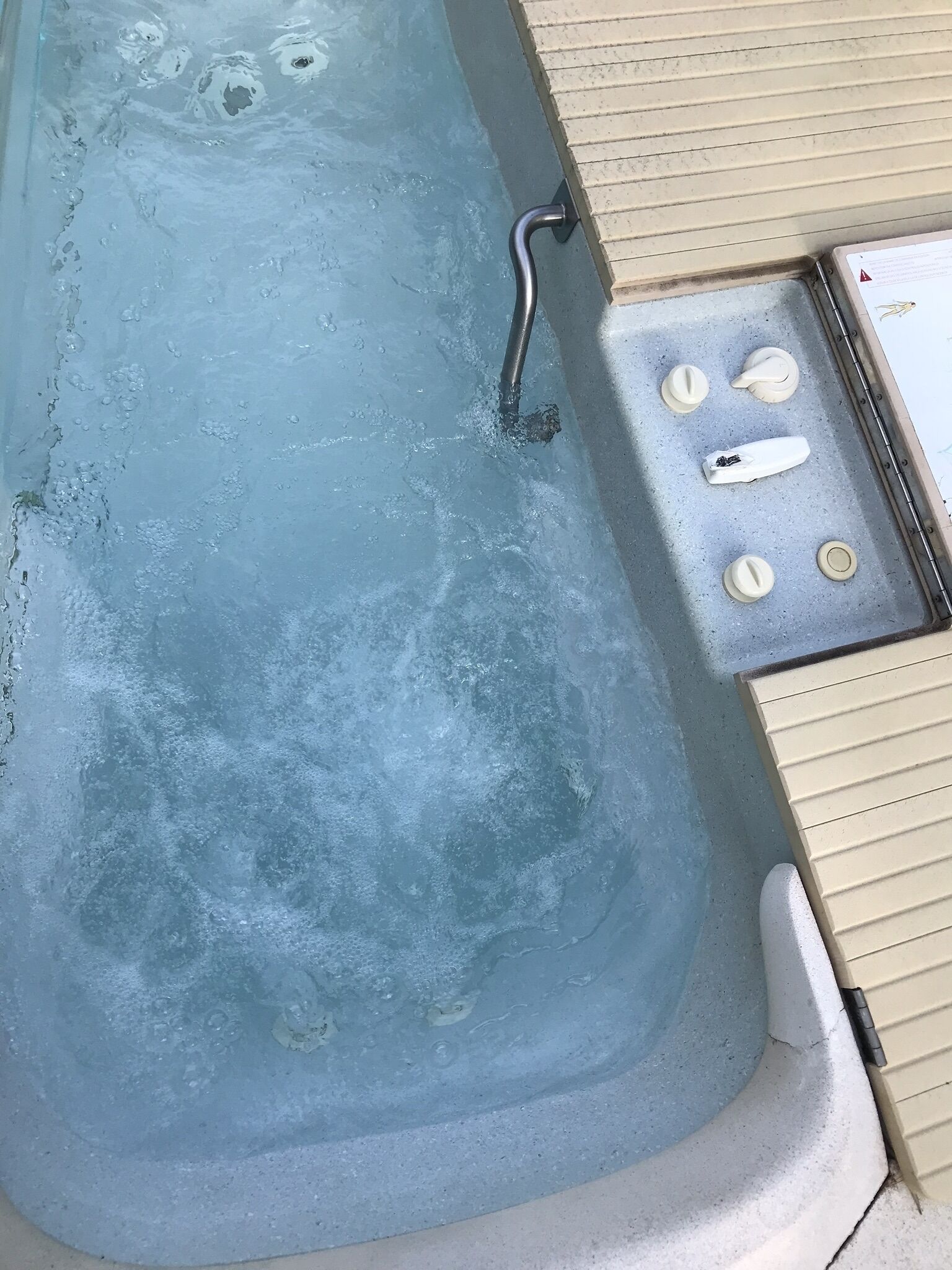 A hot tub with a metal faucet and control knobs, surrounded by beige tiles.