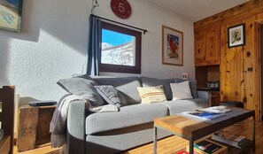 A cozy living room with a grey sofa, a wooden coffee table, and a window with a mountain view.