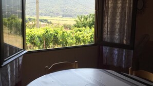 A room with a bed, a table, and a window with a view of a vineyard and mountains. - Chalet between sea and scrub  (Coggia)