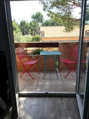 Ein Balkon mit Tisch und zwei Stühlen, ein Fliesenboden und Blick auf Bäume und Gebäude.