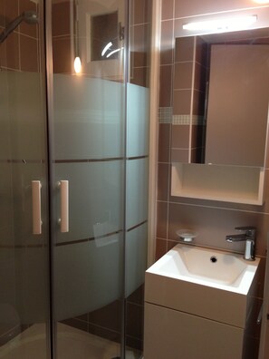 Un baño moderno con cabina de ducha de vidrio, un lavabo blanco y un espejo encima.