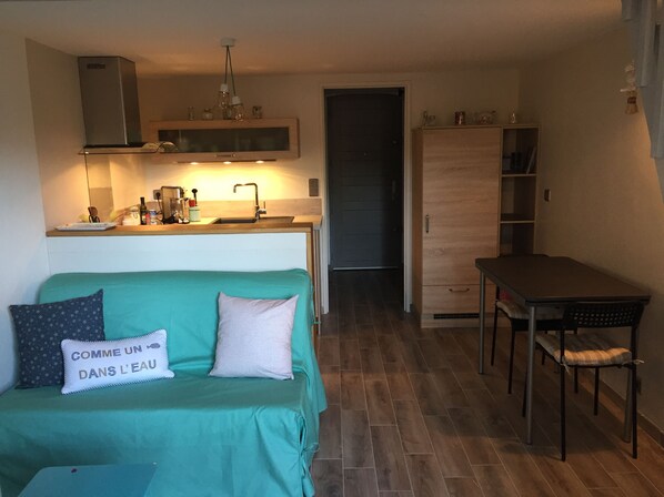 Un espacio habitable compacto con kitchenette, comedor y sofá con cojín.
