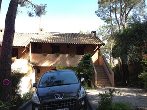 Un edificio rústico con techo de tejas, una escalera que lleva a la entrada y un coche estacionado en la parte delantera.