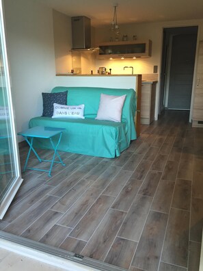 Ein gemütlicher Wohnbereich mit einem türkisfarbenen Sofa, einem kleinen Tisch und einer Küche im Hintergrund.