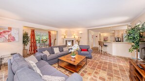 A spacious living room with a grey sectional sofa, a wooden coffee table, and a kitchen area visible in the background. - Villa in Cannes 300 meters form the sea - 5 bedrooms, garden and swimming pool (Cannes)