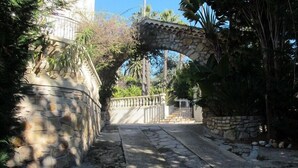 A stone pathway leading through an arched stone bridge, surrounded by lush greenery and a stone wall. - Villa in Cannes 300 meters form the sea - 5 bedrooms, garden and swimming pool (Cannes)