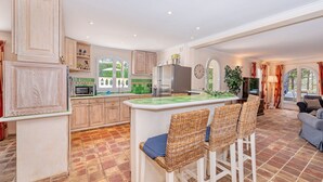 A spacious kitchen with a central island, wooden cabinets, and a dining area with wicker chairs. - Villa in Cannes 300 meters form the sea - 5 bedrooms, garden and swimming pool (Cannes)