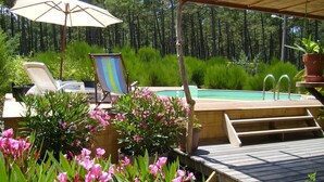 A wooden deck with a hot tub, surrounded by lush greenery and pink flowers.