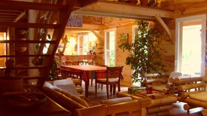 A cozy wooden cabin interior with a dining area, seating, and a large plant.