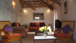 A cozy living room with wooden furniture, a television, and a vase with flowers on a table. - Traditional Provencal gite, offering quietness and serenity (Mazan)