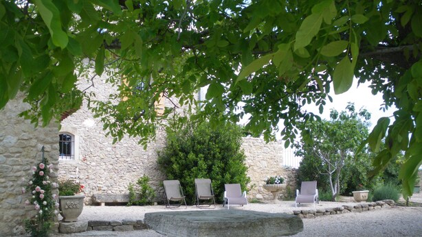 A stone building with a gravel courtyard, three stone benches, and two chairs under a tree. - Traditional Provencal gite, offering quietness and serenity (Mazan)