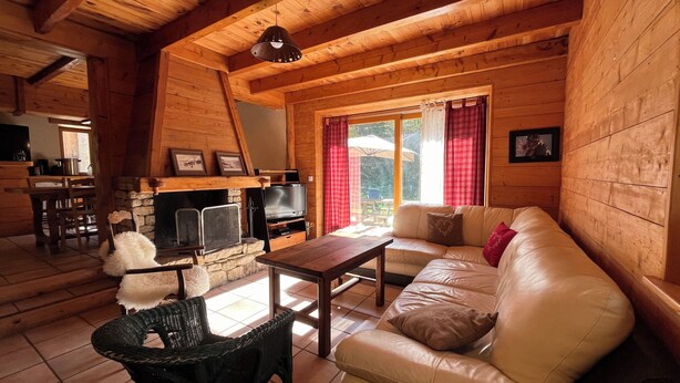 Un interior cálido de cabaña con chimenea de piedra, un sofá, una mesa de comedor y un televisor.