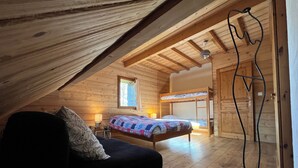 Un dormitorio acogedor en el ático con una cama litera, una cama individual, vigas de madera, un ventanal y una lámpara.