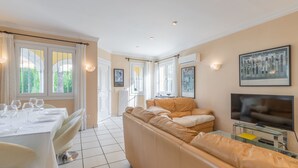 A living room with a beige sofa, a dining table set with glasses and cutlery, and a flat-screen TV mounted on the wall. - Oliva Nova Golf pool, private garden, ADSL-Wifi, TV SAT and offerts 2013 (Oliva)