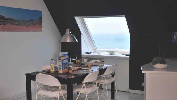 Eine kompakte Küche mit Essbereich, mit einem Fenster und Meerblick, einem Esstisch mit Stühlen und verschiedenen Küchenutensilien.