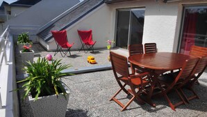 Eine Dachterrasse mit einem Holztisch und Stühlen, roten Klappstühlen, Topfpflanzen und einem Spielzeugauto.