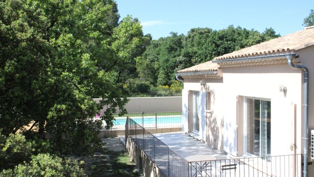 A building with a balcony overlooking a swimming pool, surrounded by trees.