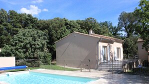 A swimming pool with a small building adjacent to it, surrounded by trees and a fenced area.