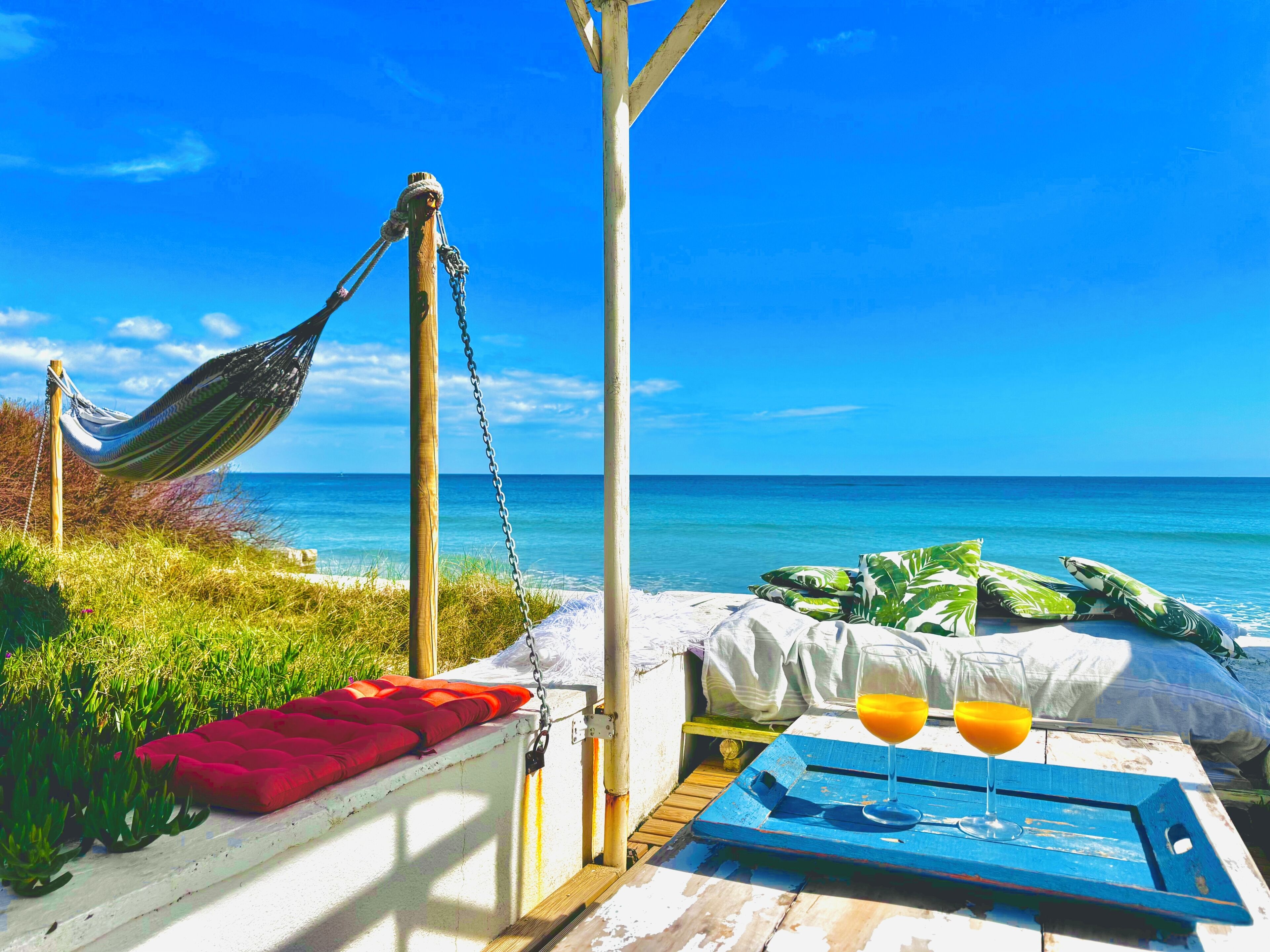 A hammock, a bed with pillows, a table with a tray, and a glass of orange juice.